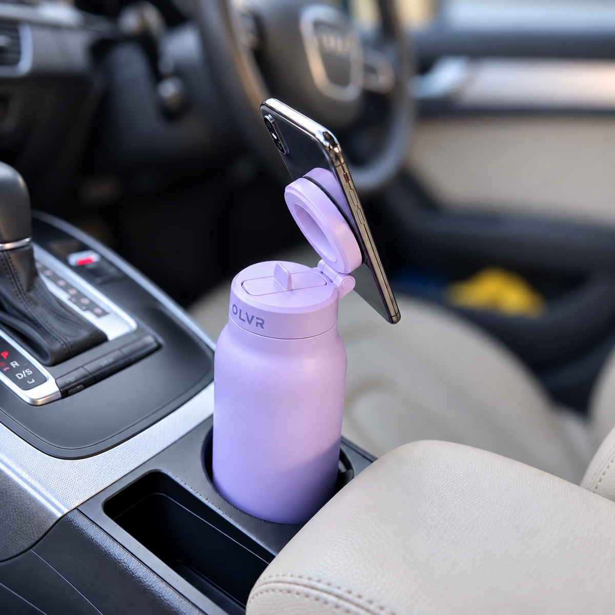 A light purple insulated water bottle with a flip-up lid and a phone mounted on top, placed in a car cup holder. 