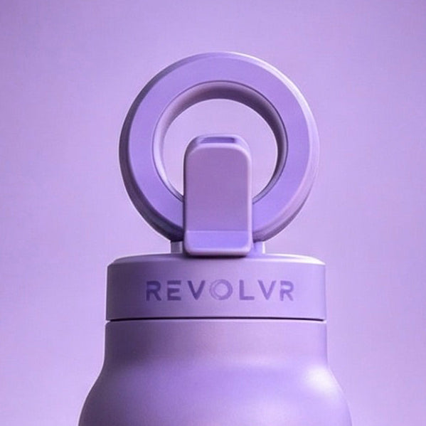 A matte lavender-purple insulated water bottle with a matching carrying loop lid, standing upright on a matching purple surface against a purple gradient background. The brand name 'REVOLVR' is printed on the neck of the bottle.
